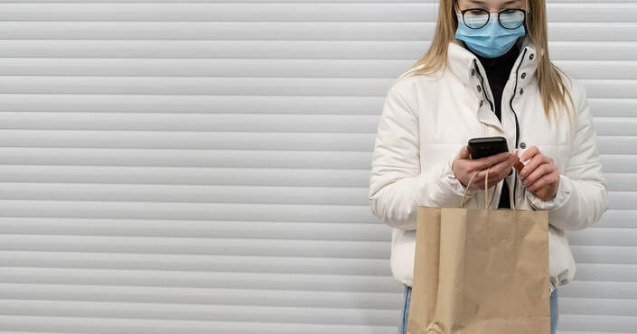 A woman wearing a face mask is making an online payment via mobile phone